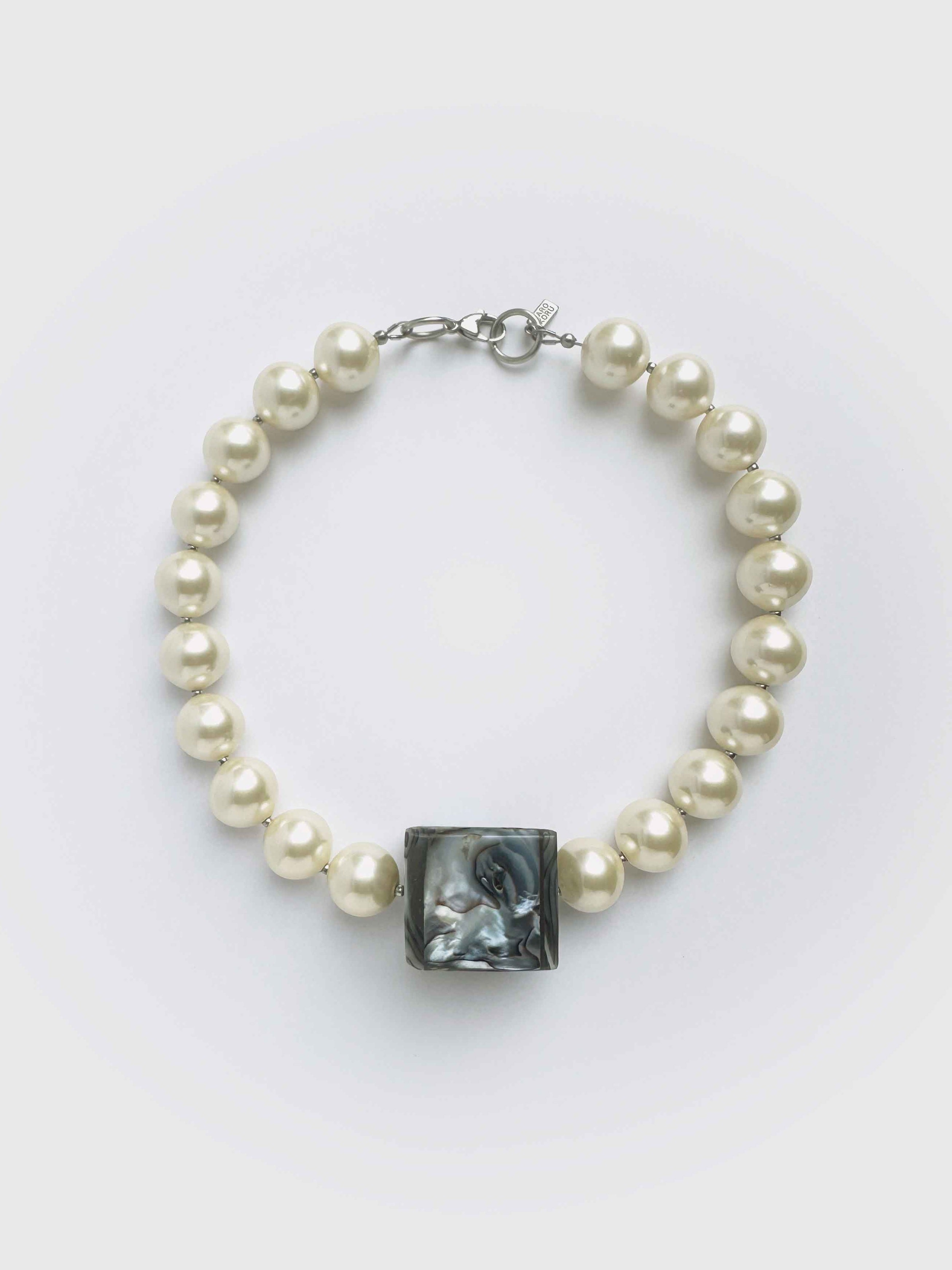 Pearl necklace with a central black square stone on a white background