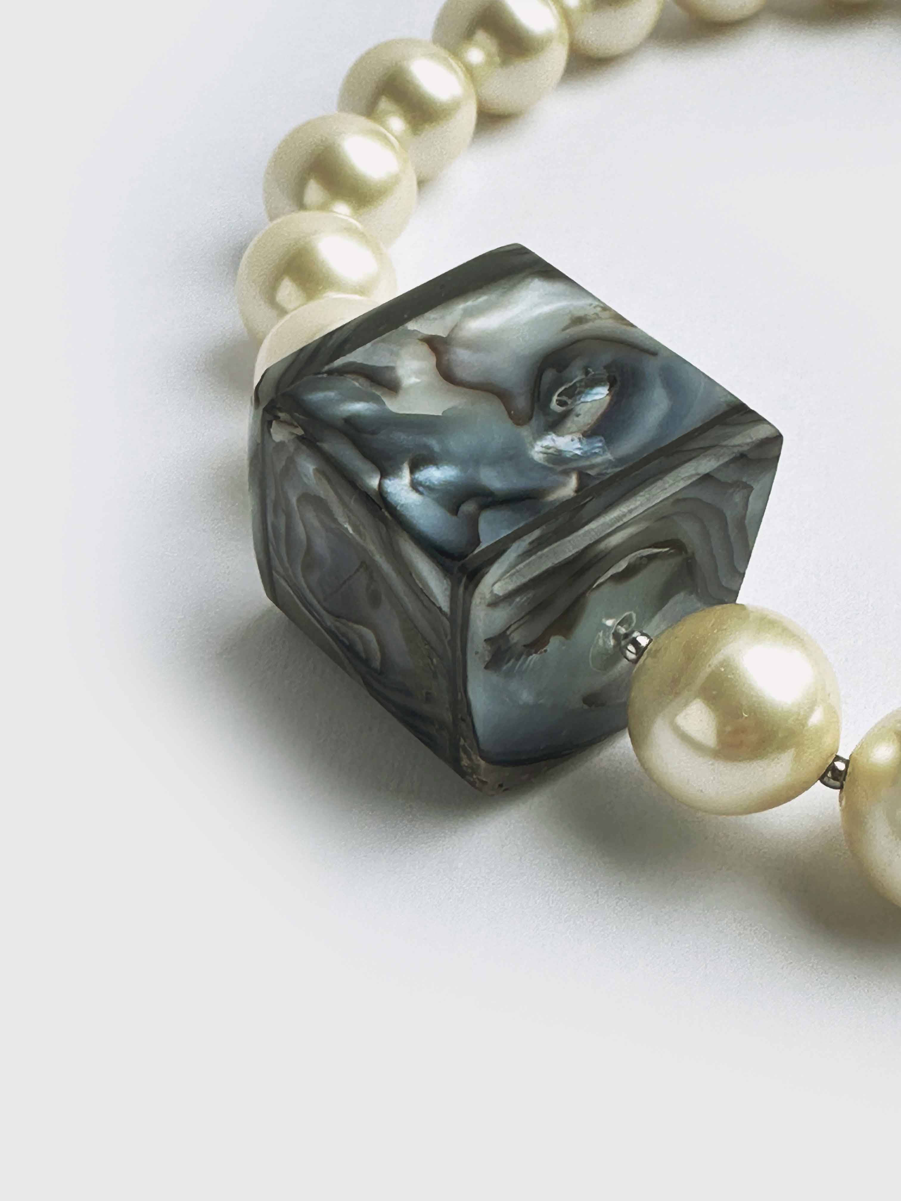 Necklace with a cube-shaped gray and white bead and pearl beads on a light background