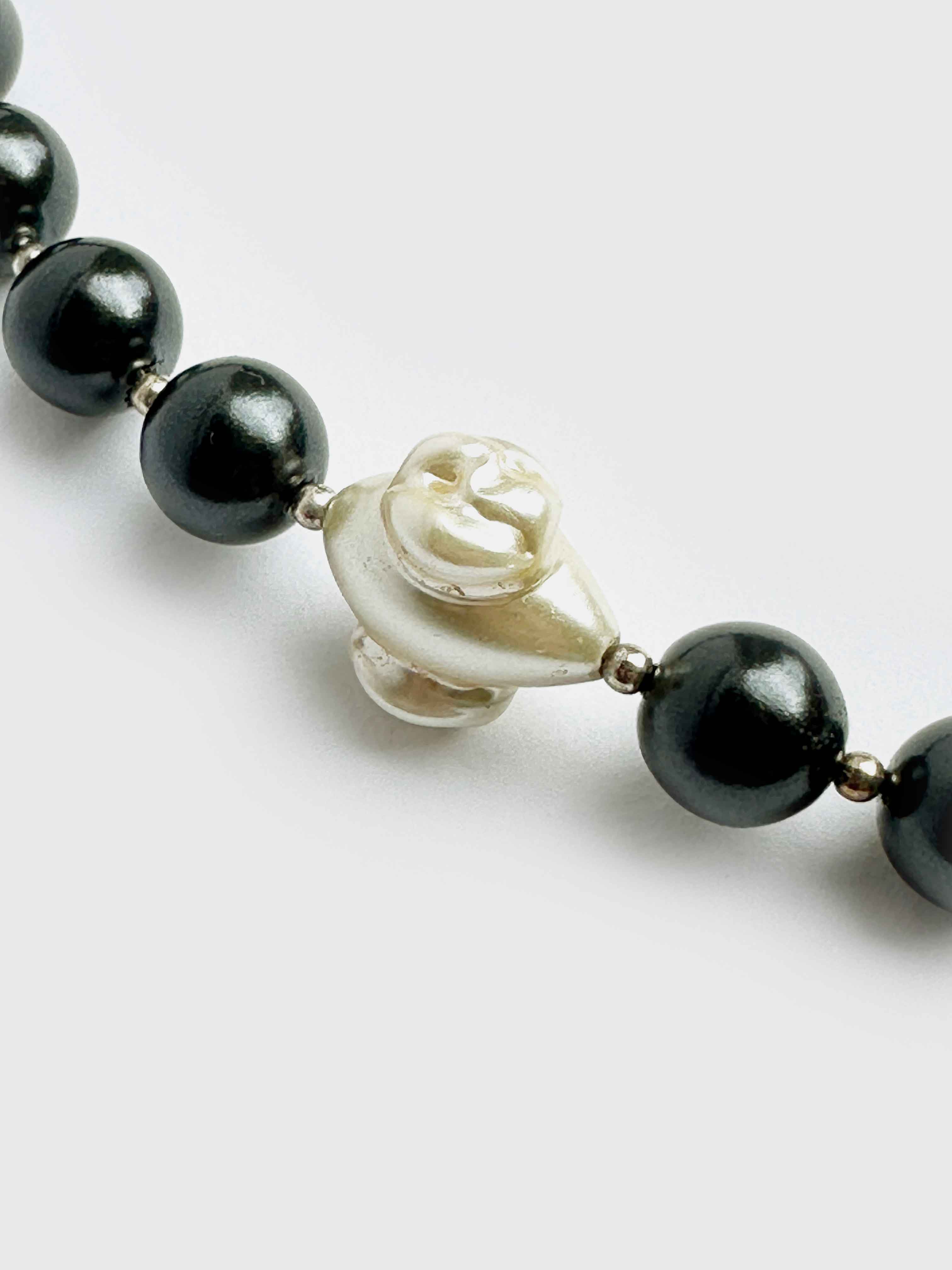 Necklace with black pearls and a white rose-shaped bead on a light gray background