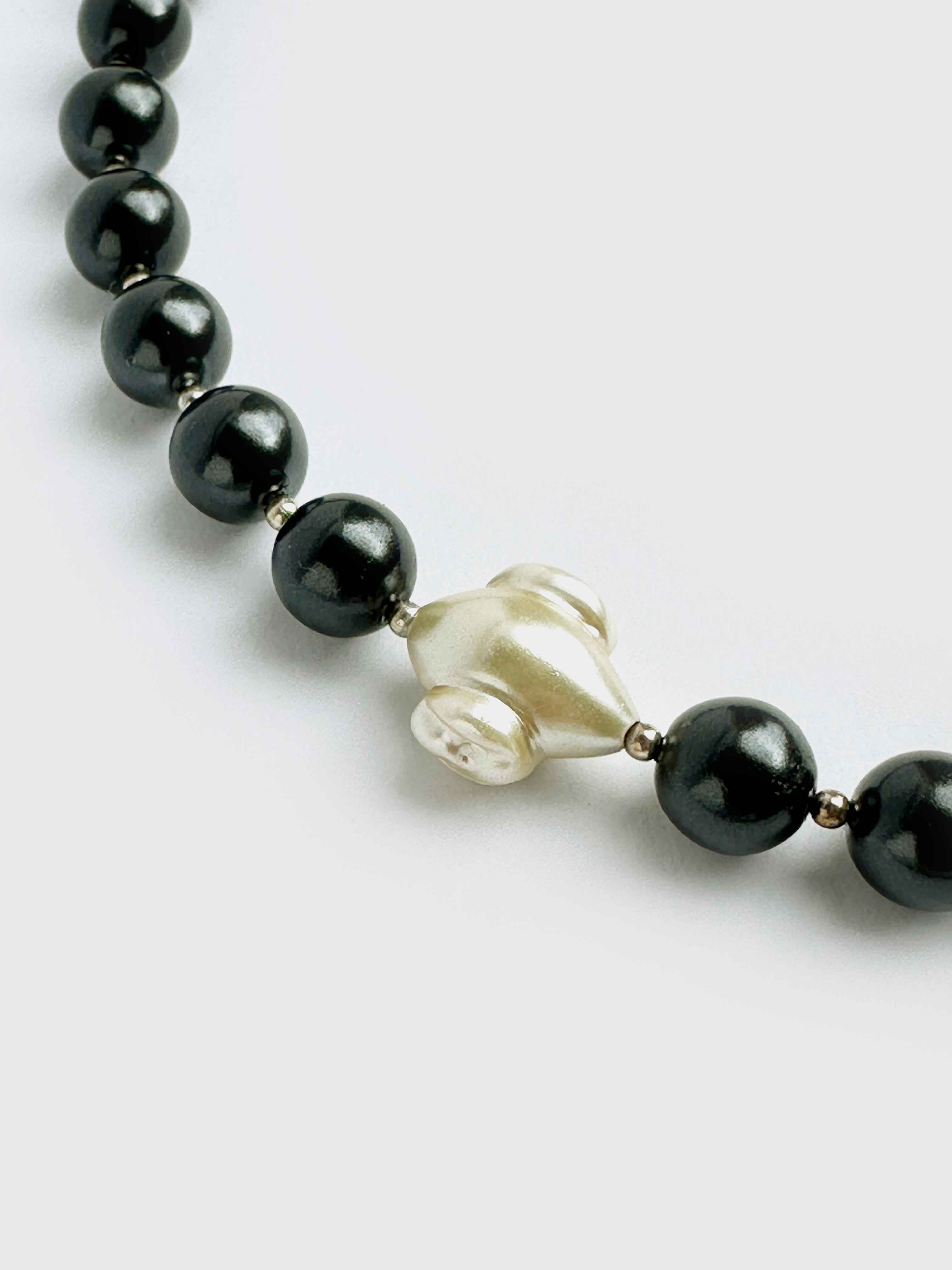 Necklace with black beads and a central white pearl on a light gray background