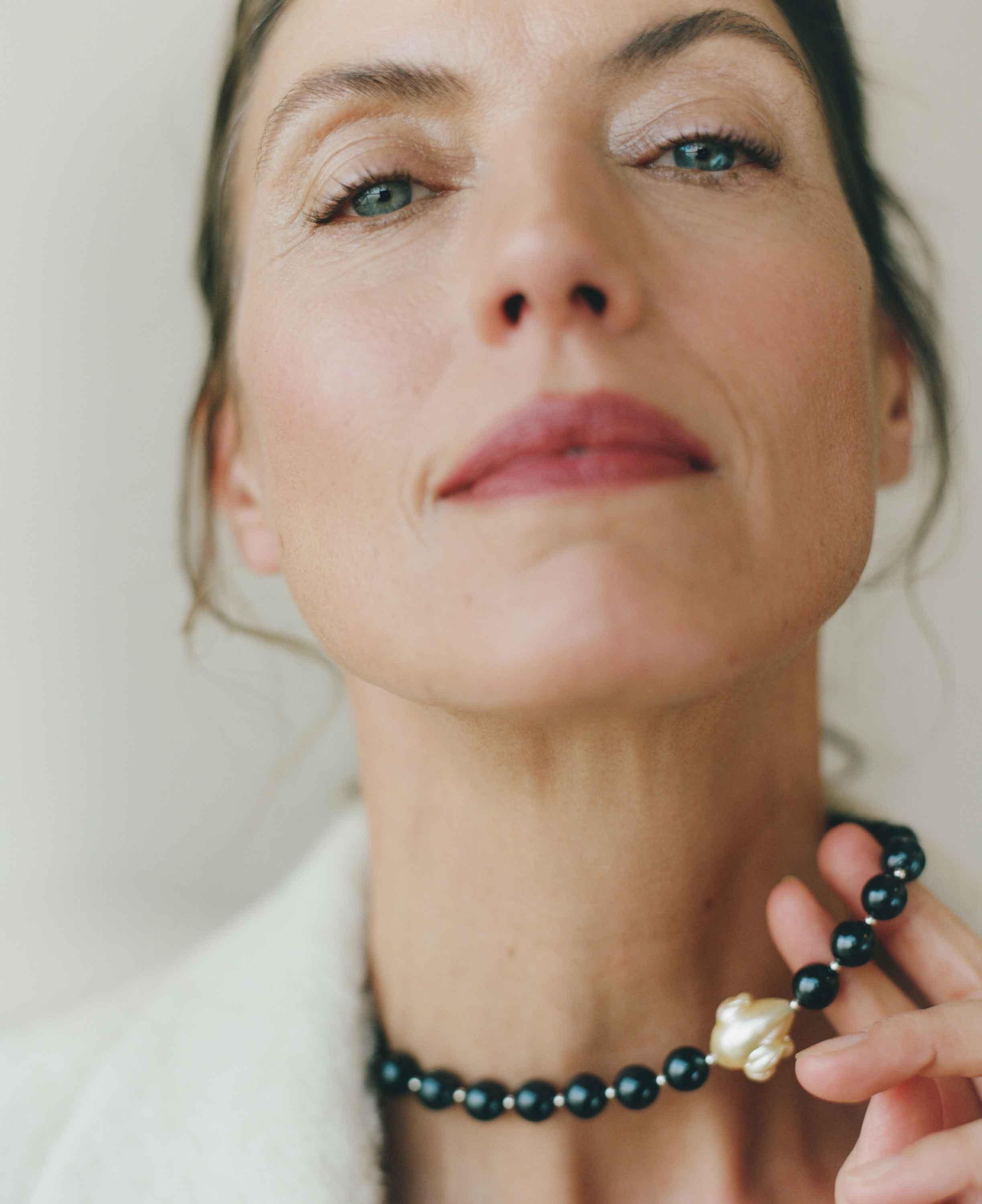 Woman wearing a black beaded necklace with a gold clasp against a neutral background