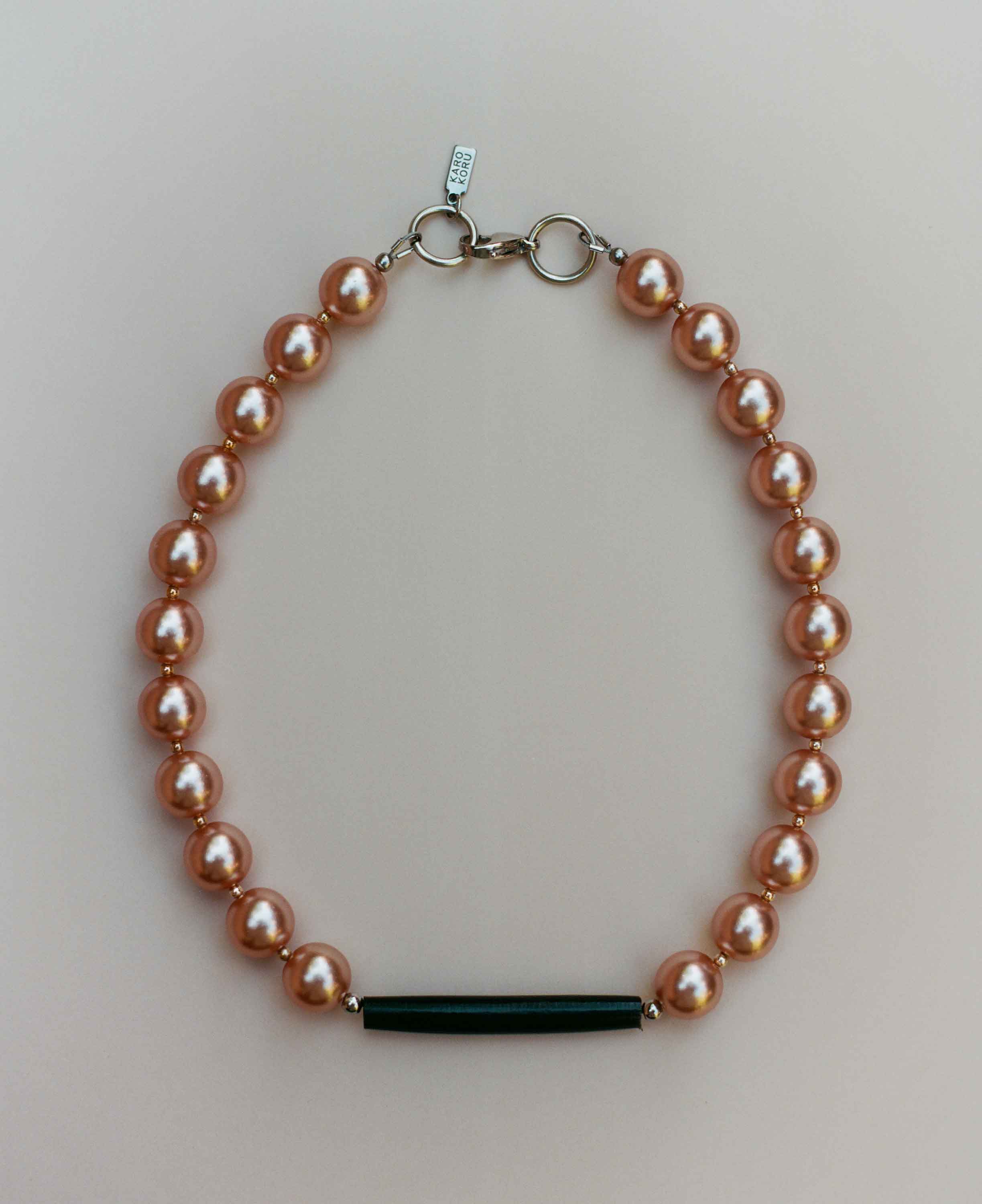 Pearl bracelet with a black bar clasp on a light gray background