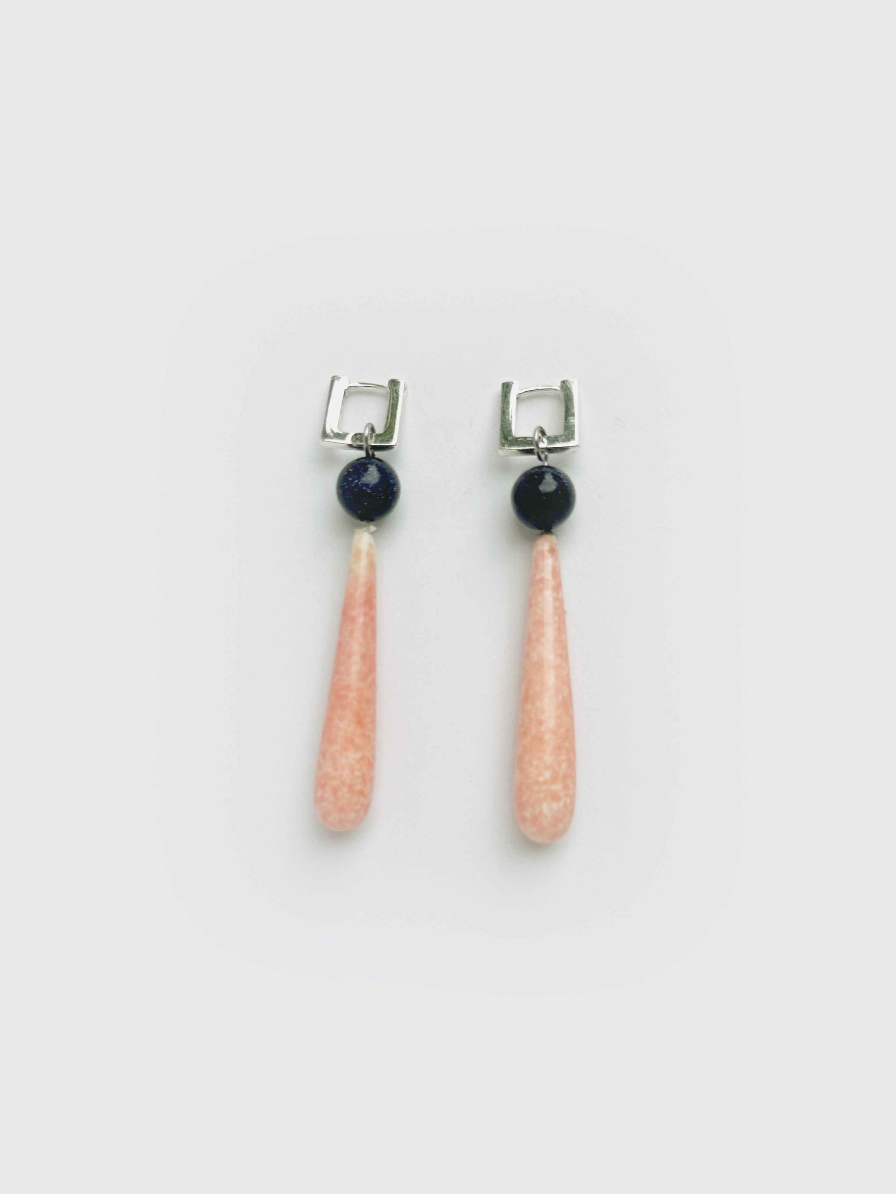 Pair of earrings with pink teardrop-shaped stones and black beads on a white background