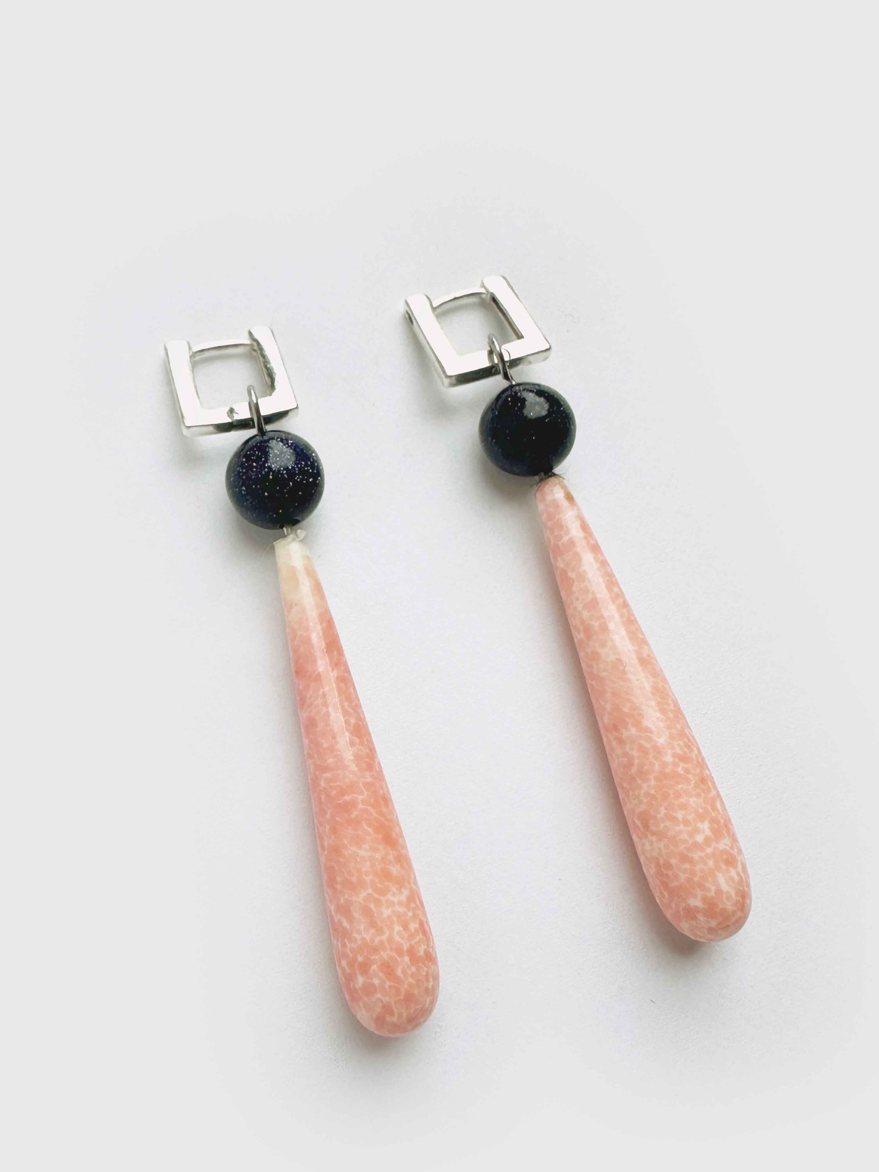 Pair of earrings with pink teardrop-shaped stones and black beads on a light gray background