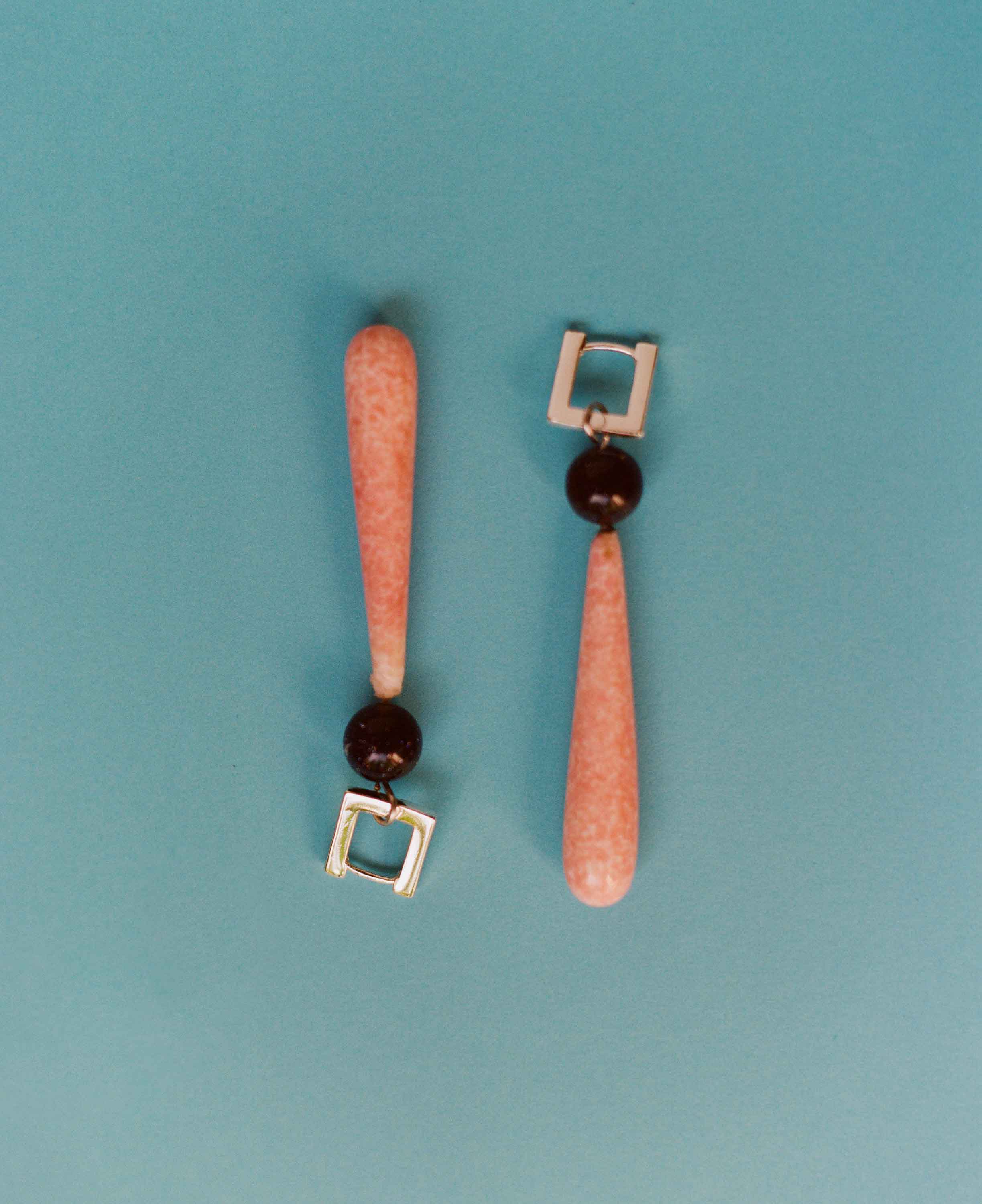 Pair of earrings with coral-like pink beads and dark beads on a teal background