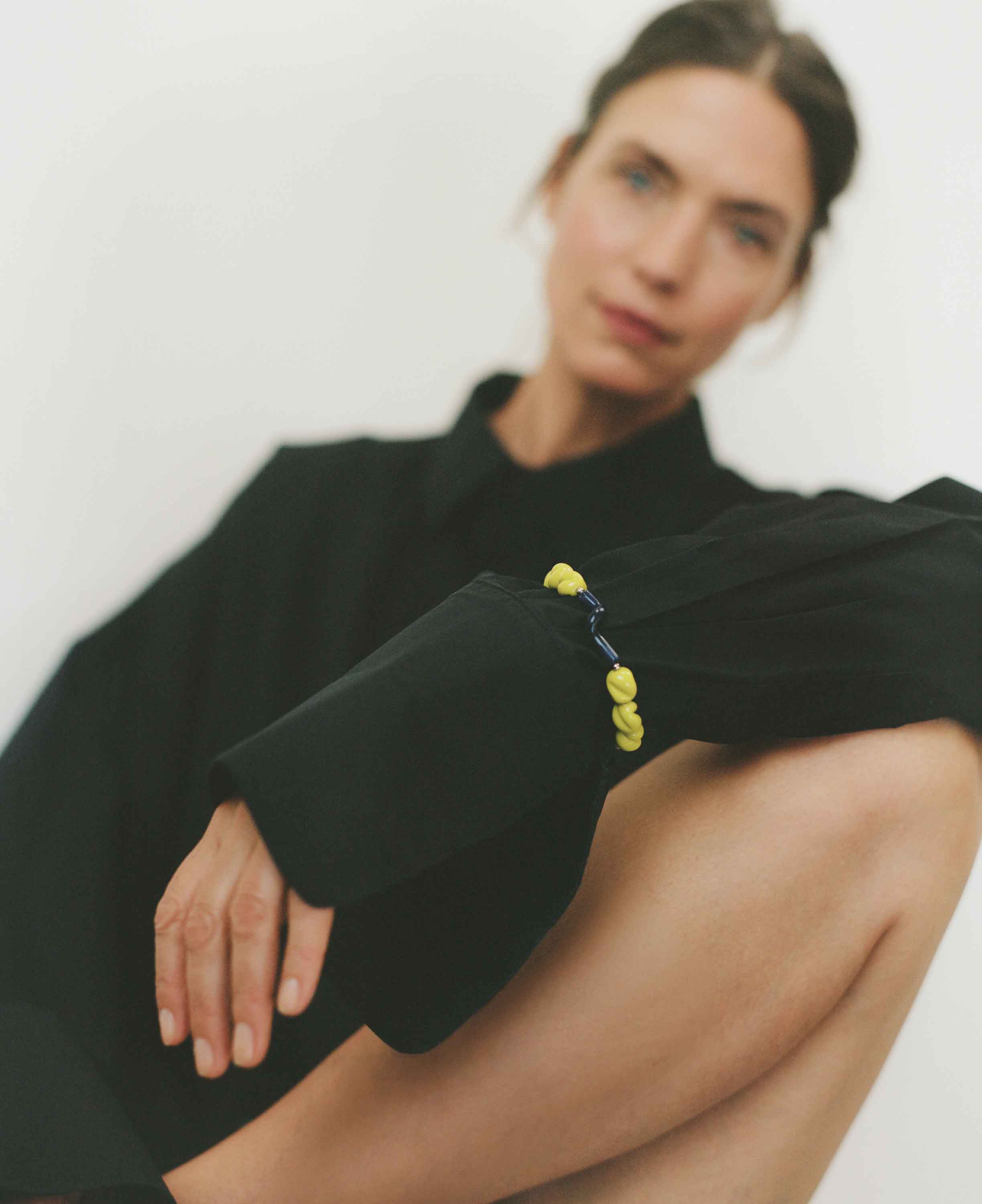 Person wearing a black outfit with a yellow beaded bracelet on a white background