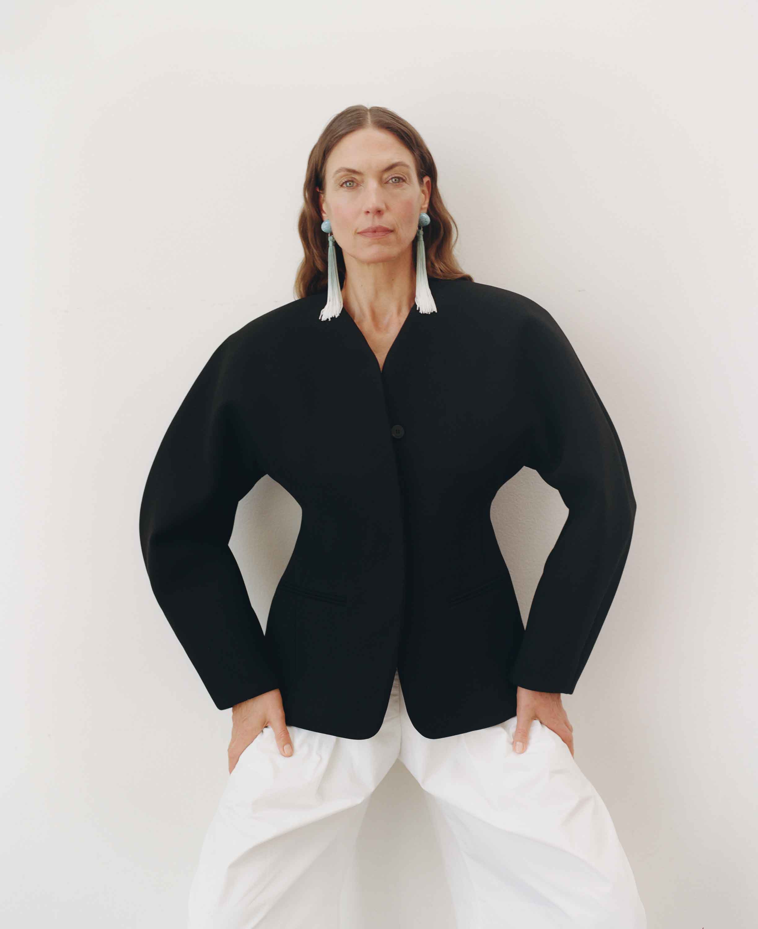 Person wearing a black jacket and white pants against a plain background