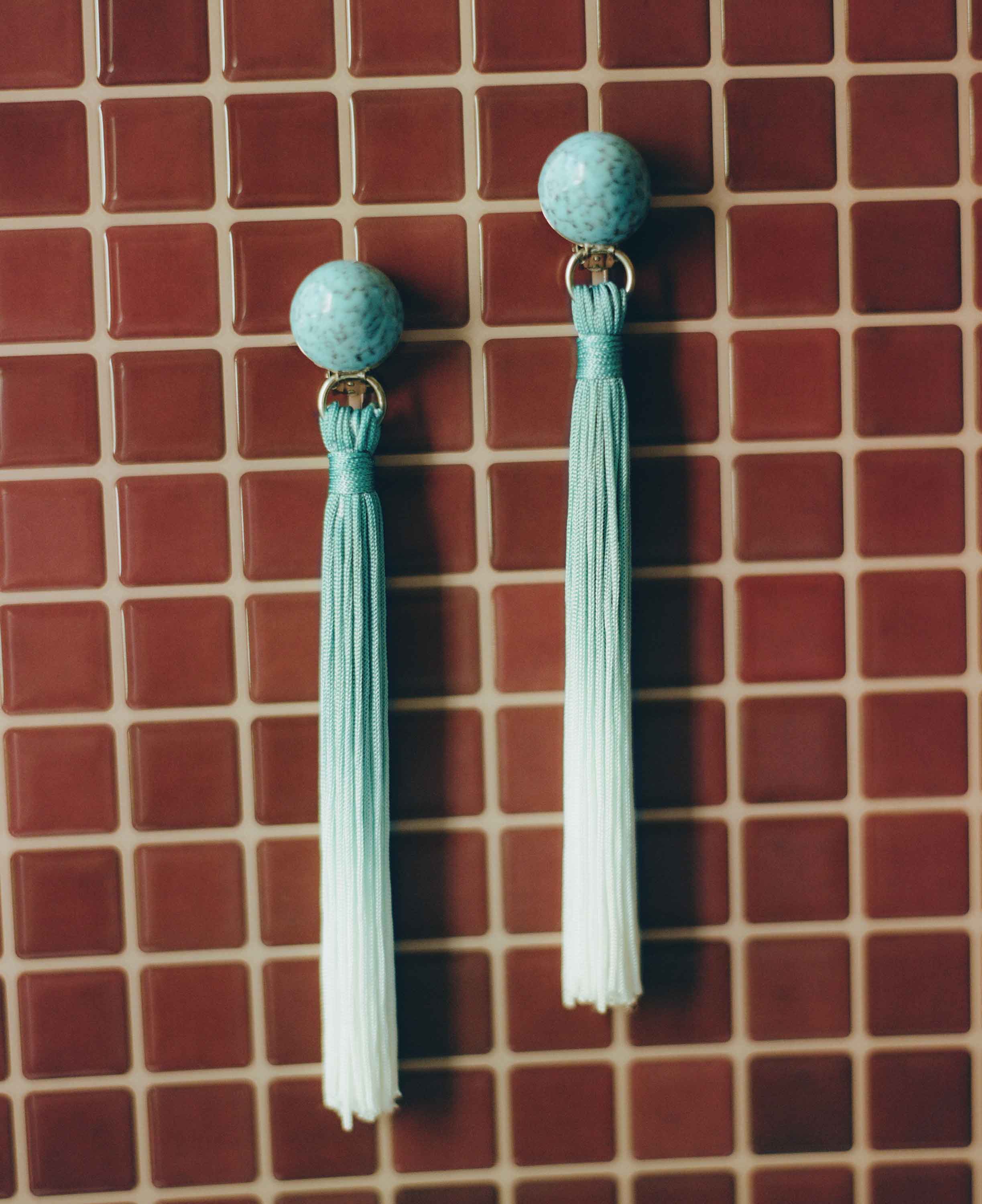 Pair of turquoise earrings with tassels on a red tiled background