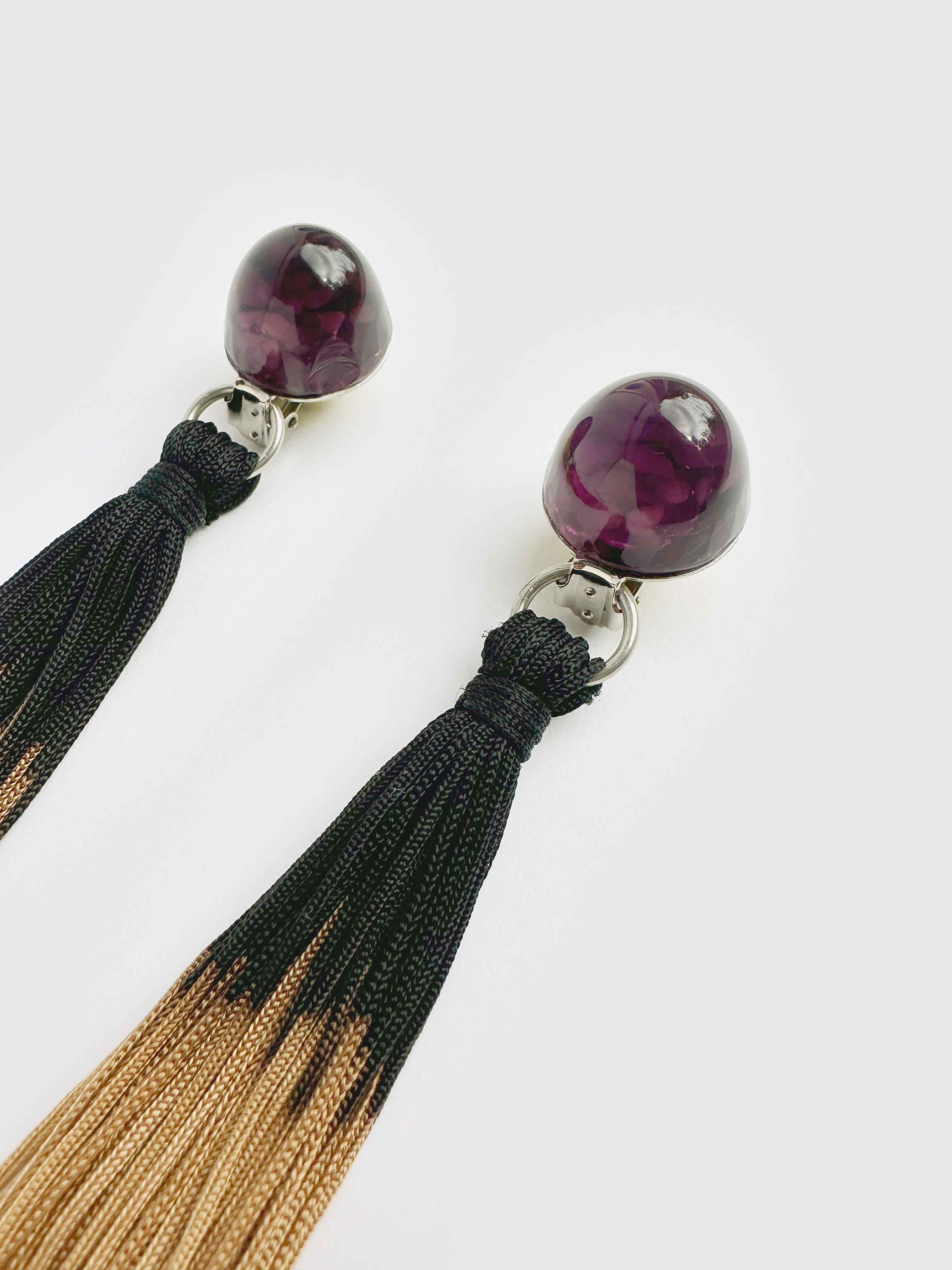 Pair of earrings with purple gemstones and black and gold tassels on a white background