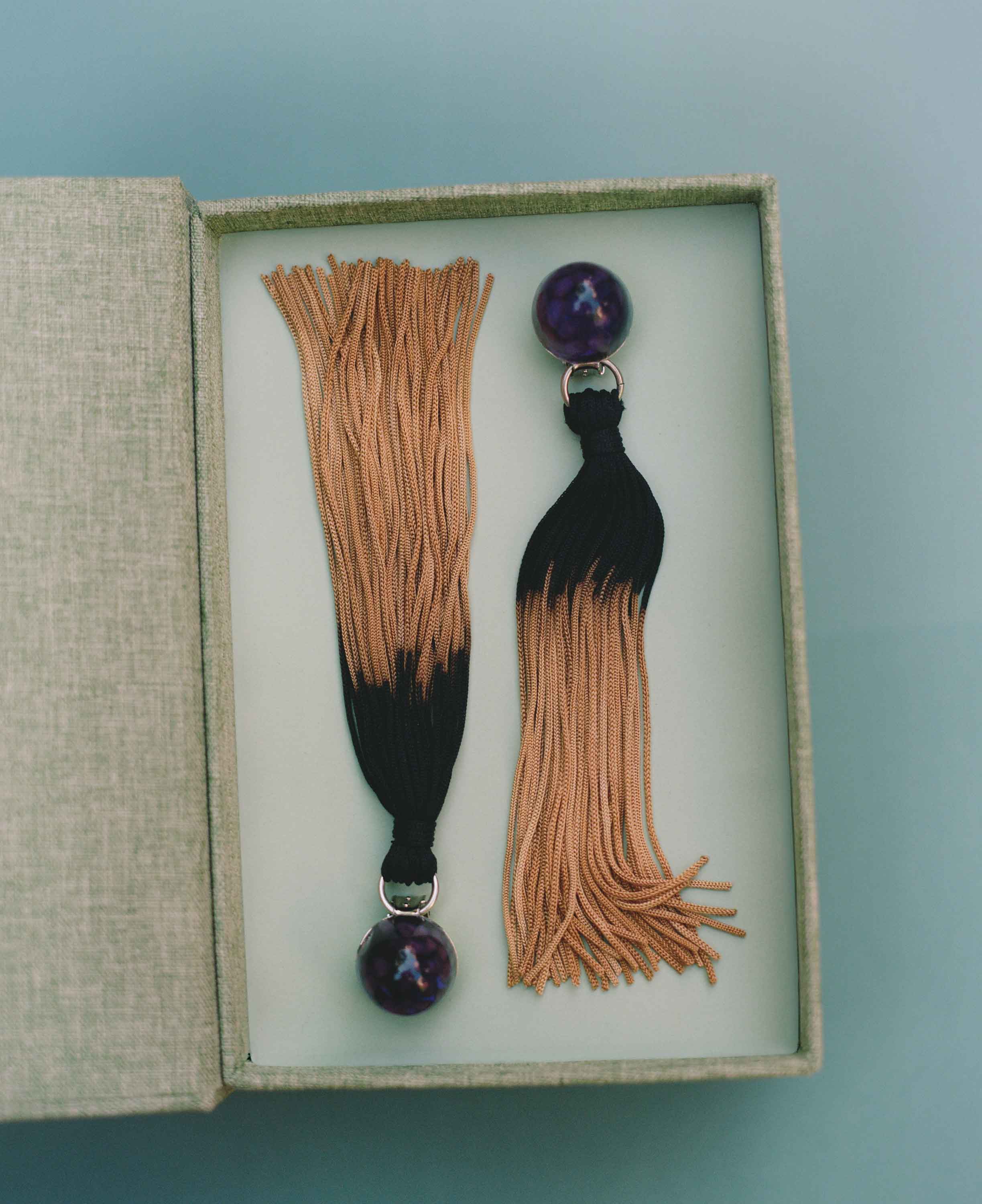 Pair of tassel earrings with purple beads in a box on a light blue background