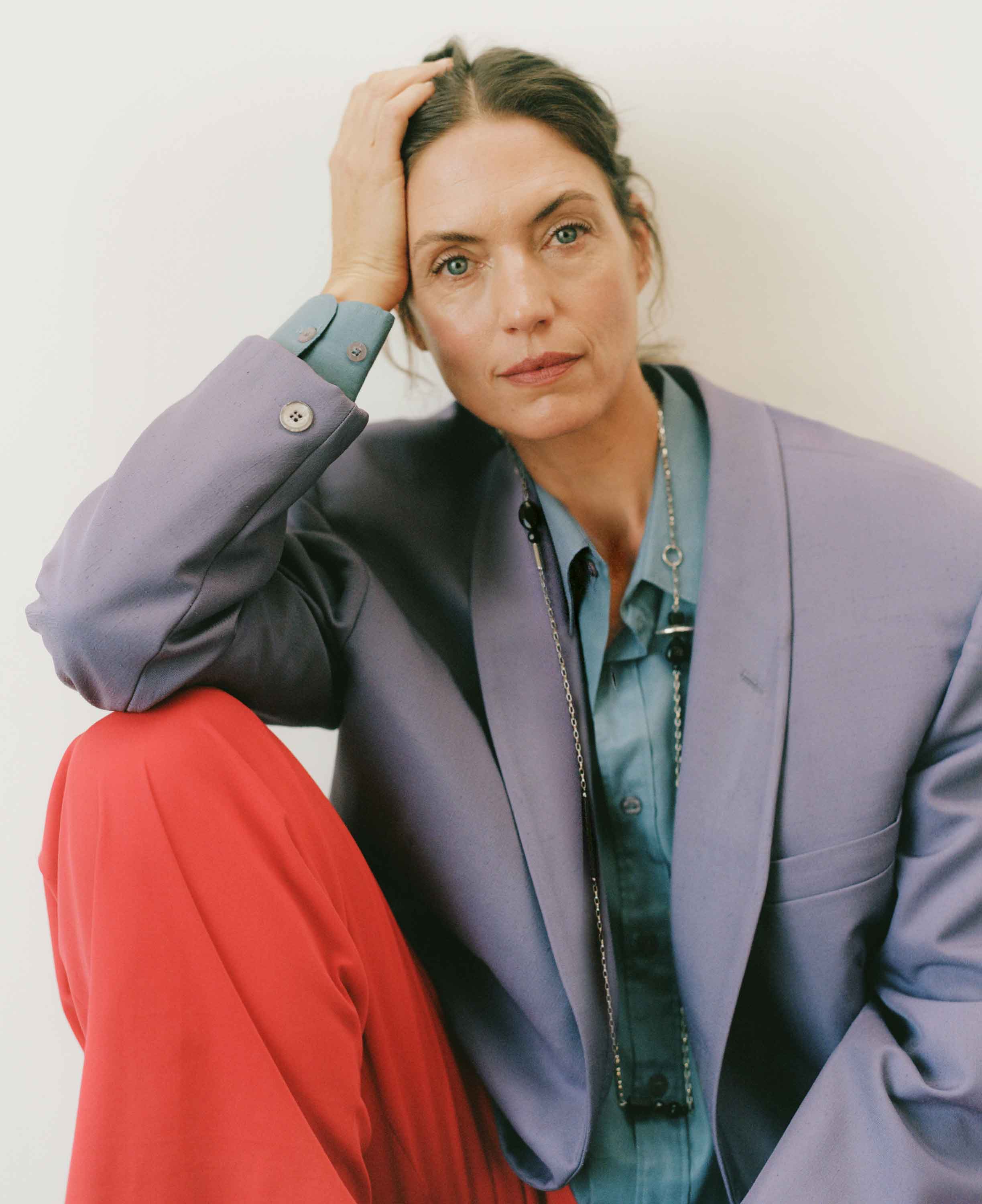 Woman wearing a light purple blazer over a red garment with a plain background