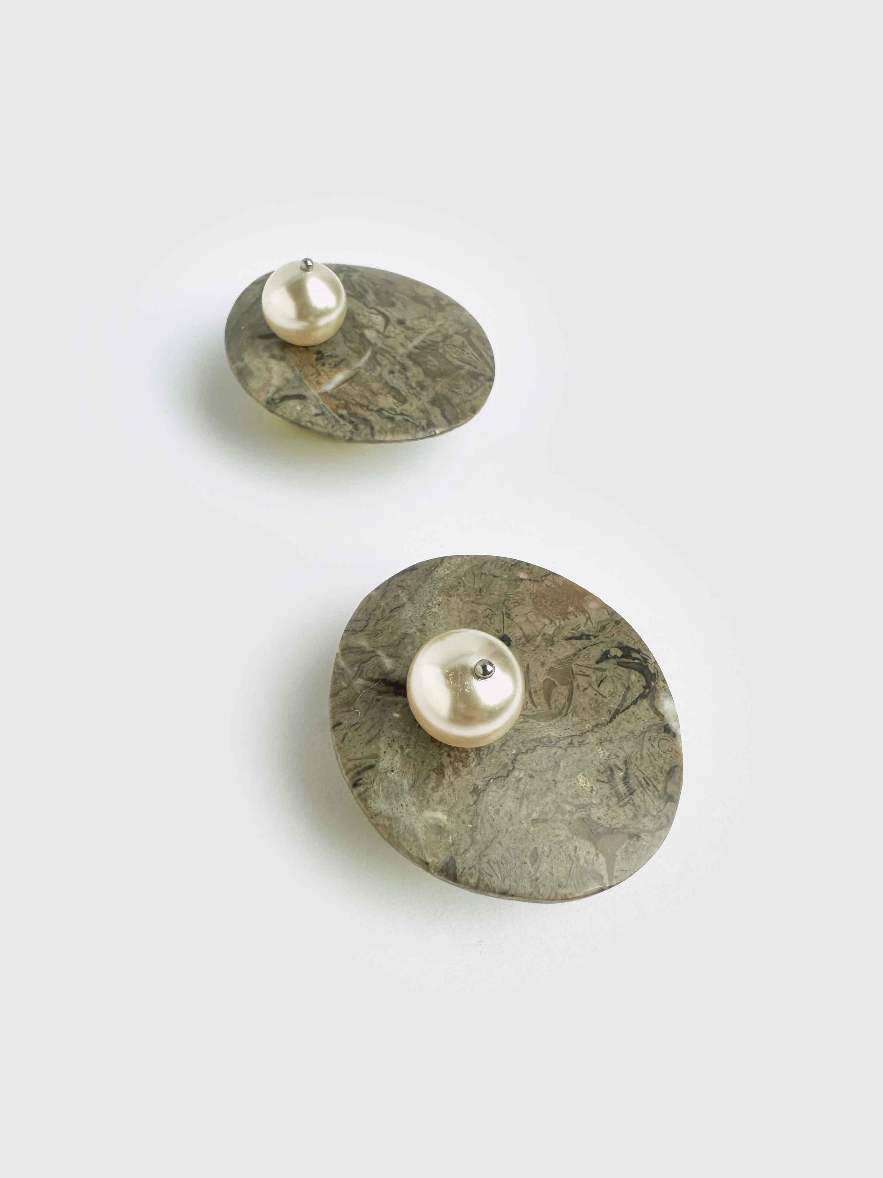 Pair of earrings with round stone-like bases and pearl centers on a light gray background