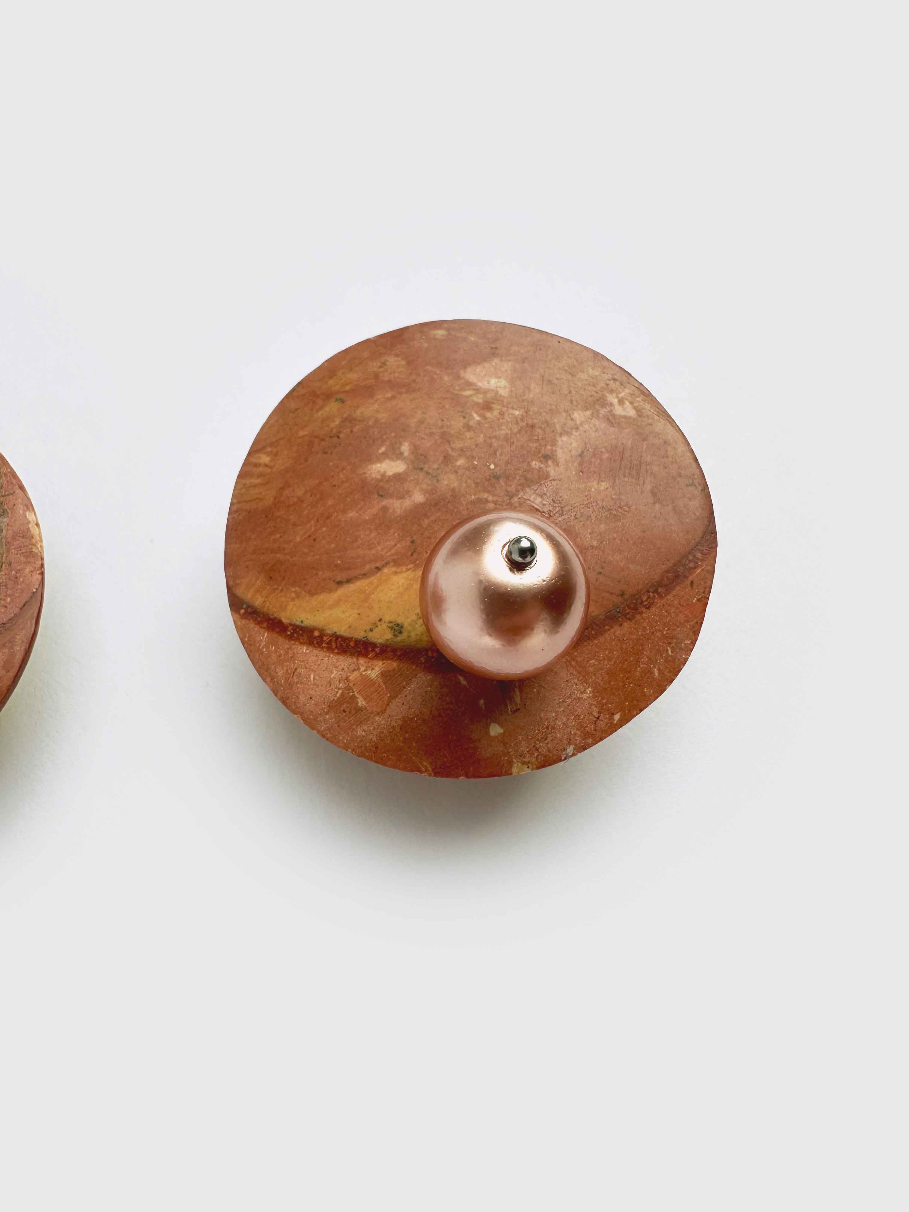 Brown stone like disc earrings with pearls on white background.