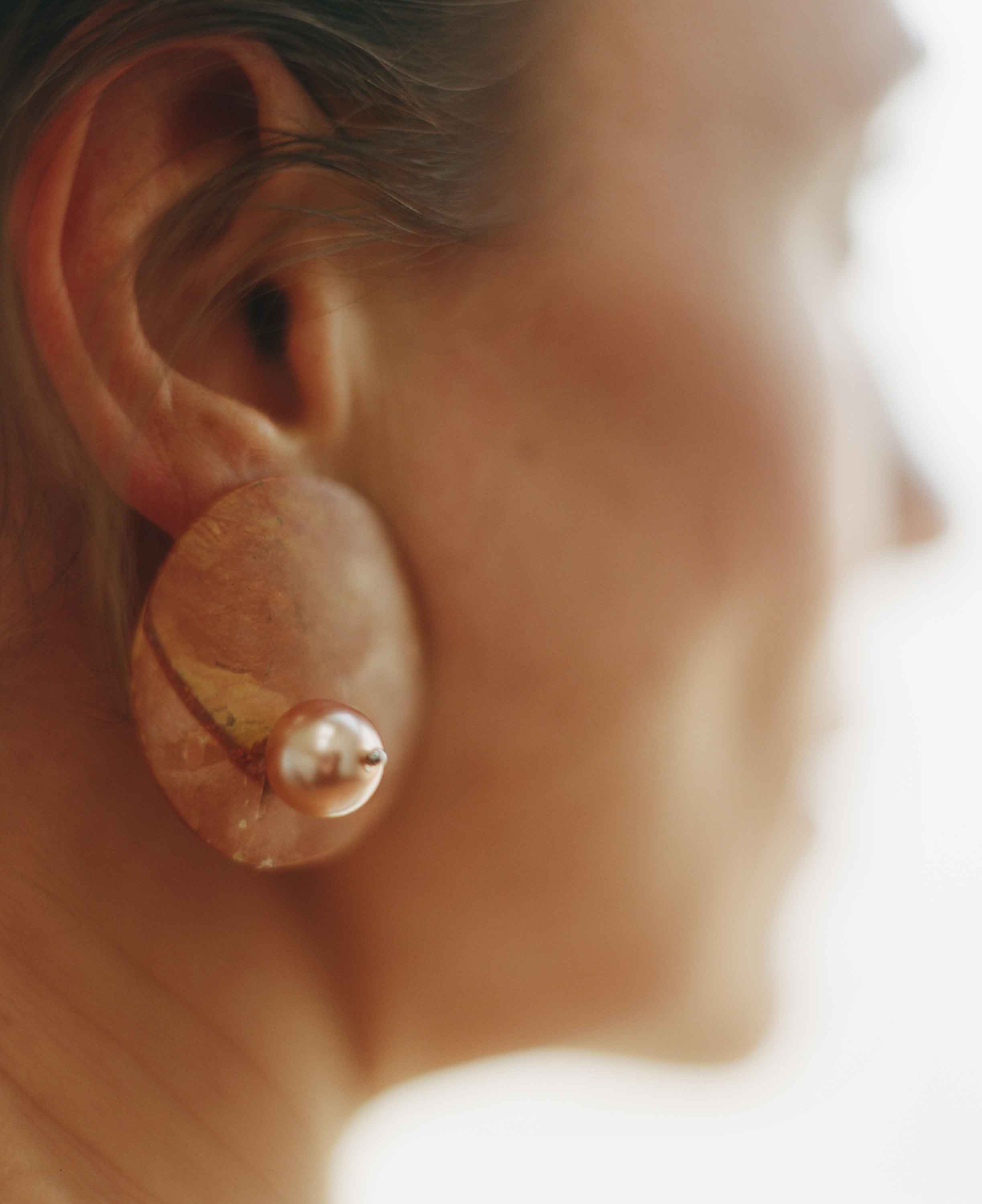 Close-up of a person wearing a gold earring with a blurred background